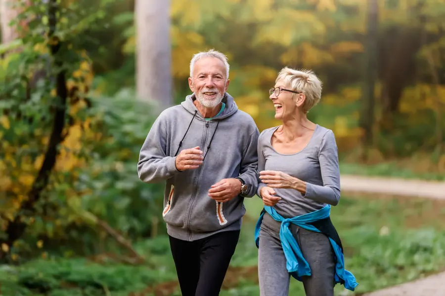 An older couple jogging together outdoors, laughing.