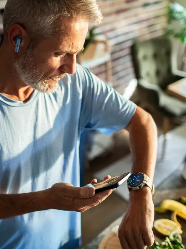 A man in his kitchen, checking the LifeLeaf app on his wrist beside the food he is preparing.