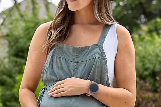 A pregnant woman outdoors wearing LifeLeaf, hand resting on her bump.